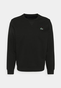 Černá mikina vyrobená z bavlněné směsi. Má kulatý výstřih, dlouhé rukávy a malé zelené logo Lacoste na hrudi. Měkká textura.
