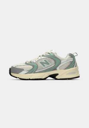 Białe i jasnoszare sneakersy sportowe New Balance z siateczkowym materiałem, beżową podeszwą i czarnym bieżnikiem, pokazane z boku na jednolitym tle.