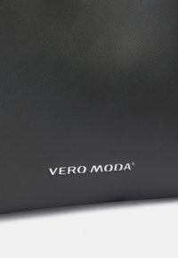 Sac en simili cuir noir texturé avec un logo "VERO MODA" blanc en bas. La surface est lisse avec un léger motif de grain.