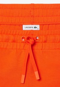 Klarröda shorts med dragsko i midjan, med en liten Lacoste-etikett och en slät, mjuk textur.