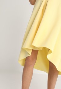 Vestido amarillo asimétrico con tejido fluido. El dobladillo es más corto en la parte delantera y más largo en la parte trasera, creando un efecto de capas.