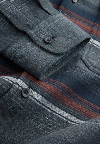 Camicia con bottoni in tessuto strutturato, base blu navy con righe contrastanti rosse e bianche, con bottoni neri e motivo a spina di pesce.