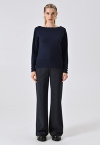 Marineblauer Strickpullover mit weitem Ausschnitt und langen Ärmeln, kombiniert mit dunkelgrauen weit geschnittenen Hosen und schwarzen Plateauschuhen.