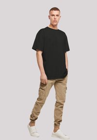 Zwarte T-shirt met korte mouwen en een relaxte pasvorm, gecombineerd met beige cargobroeken met zijzakken en elastische boorden. Gecombineerd met witte sneakers.