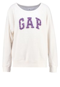 Weißer Pullover mit weitem Ausschnitt und langen Ärmeln. Auf der Vorderseite prangt „GAP“ in strukturierten lila- und pinkfarbenen Buchstaben. Bündchen und Saum sind gerippt.