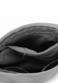 Offene Handtasche mit schwarzem und weißem gewelltem Innenfutter, das sowohl Reißverschluss- als auch offene Fächer zeigt.