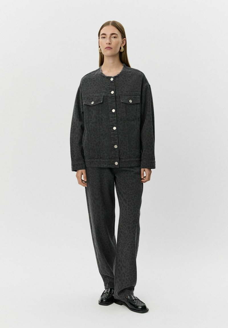 Siva denim jakna z leopardjim vzorcem, ki ima dve sprednji žepni in srebrne gumbe. V kombinaciji z ujemajočimi se hlačami in črnimi čevlji.