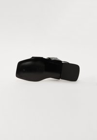 Black heeled shoe with a smooth texture, rectangular heel, and adjustable buckle detail; features a ribbed sole for traction.