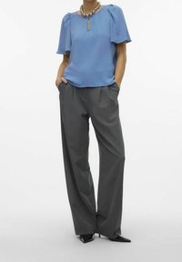 Blusa azzurro chiaro con maniche a palloncino corte e dettaglio a forma di chiave sul collo; pantaloni grigi a vita alta e gamba larga; tacchi neri a punta.