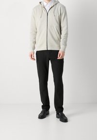 Felpa con cappuccio grigio chiaro con cerniera frontale e tasche anteriori, abbinata a pantaloni neri a gamba dritta e mocassini neri.