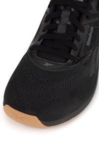 Čierna atletická obuv s textúrovaným sieťovým vrškom, syntetickými akcentmi, čiernymi šnúrkami a gumovou podrážkou s hnedým hrotom. Branding viditeľný na boku.