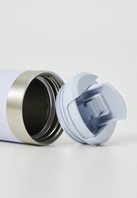 White insulated stainless steel bottle with a detached light blue plastic flip-top lid lying on a white surface.