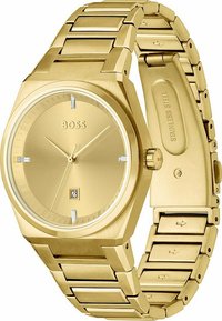 Reloj de acero inoxidable dorado con una esfera cuadrada, diseño minimalista y display de fecha a las 6 en punto. Presenta una pulsera de eslabones.