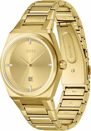 Montre en acier inoxydable doré avec un cadran carré, un design minimaliste et un affichage de la date à 6 heures. Elle est dotée d'un bracelet à maillons.