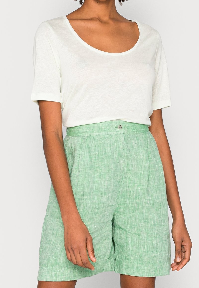 Pantaloni corti verde chiaro strutturati con vita alta e chiusura a bottone, abbinati a una morbida t-shirt crema con scollo a cuore.