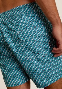 Zwemshorts met een geometrisch patroon in turquoise, zwart en wit. Voorzien van een elastische tailleband en een patchzak aan de rechterkant.