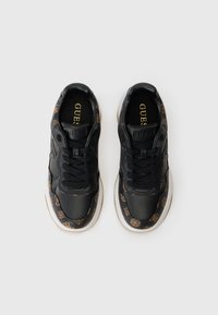 Para czarnych sneakerów marki Guess z brązowymi wzorzystymi akcentami, czarnymi sznurowadłami i białymi podeszwami, widziana z góry na białym tle.