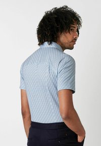 Kurzarmhemd aus leichtblauem Stoff mit geometrischem Muster, schlanker Schnitt und klassischem Kragen. Glatte Textur, minimalistische Details.