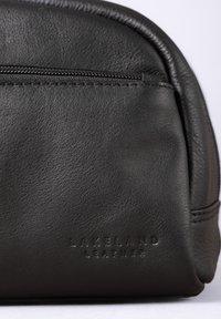 Black leather bag featuring a textured finish, zip closure, and embossed "Lakeland Leather" branding at the front. Rounded shape with stitching accents.