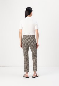 Chemise blanche à manches courtes associée à un pantalon à carreaux brun et noir, avec une coupe ajustée et une taille plate. Des sandales à brides sont portées.
