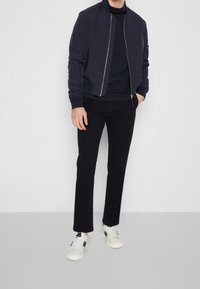 Marinblå bomberjacka med ribbstickade mudd och krage, parat med en svart polokrage, svarta byxor och vita sneakers med svarta accenter.