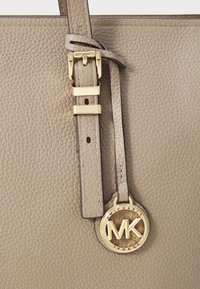 Grijze leren tote van gekorreld leer met gouden hardware, met een decoratieve MK-logo hanger en riemaccenten.