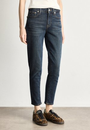 Jean en denim bleu foncé avec une coupe slim et une longueur à la cheville. Présente un design traditionnel à cinq poches et des coutures contrastées. Associé à des baskets à imprimé léopard.