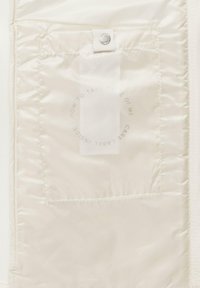 Tissu en satin blanc avec une finition brillante, présentant une fermeture à pression et une étiquette d'entretien intérieure avec du texte circulaire. Texture et éclat subtils.