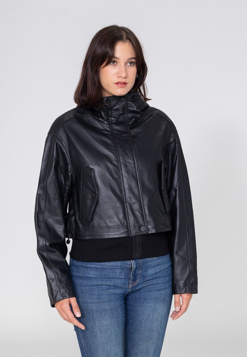 Schwarze Lederjacke in cropped Form mit hohem Kragen, durchgehendem Reißverschluss und zwei seitlichen Taschen. Glatte Textur mit minimalen Hardware-Details.