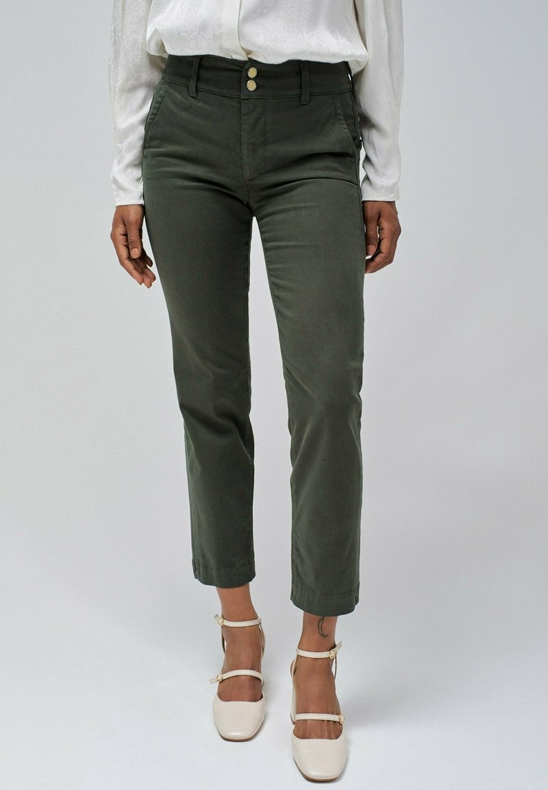 Zelené kalhoty z bavlněné směsi s vysokým pasem, dvěma předními kapsami, dvěma knoflíky a zkrácenou délkou, doplněné světle barevnými sandály na podpatku.