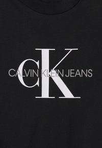 Czarna koszulka z dużym białym logo "CK" oraz napisem "CALVIN KLEIN JEANS" w czystej, nowoczesnej czcionce bezszeryfowej.