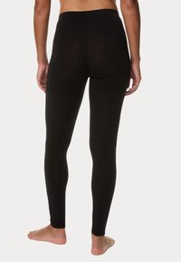 Černé legíny s vysokým pasem, hladkou texturou a přiléhavým střihem. Žádné viditelné vzory ani kování. Modelka stojí naboso.