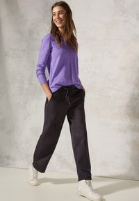 Lilla strikket sweater med rund halsudskæring, parret med sorte bukser med elastisk talje og hvide high-top sneakers. Glatte teksturer og afslappet design.