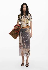 Bedrukt topje met meerdere patronen en korte mouwen, gecombineerd met een transparante, lange rok met bloem- en abstracte ontwerpen. Bruine en rode accentjasje.