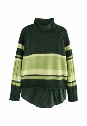 Persona vistiendo un suéter de lana a rayas en tonos verde oscuro y verde claro sobre una camisa larga verde oscuro, vista desde atrás contra un fondo marrón.