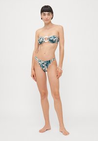Bikini set featuring a strapless top with a circular white accent and floral pattern in teal and beige, paired with matching low-rise bottoms.