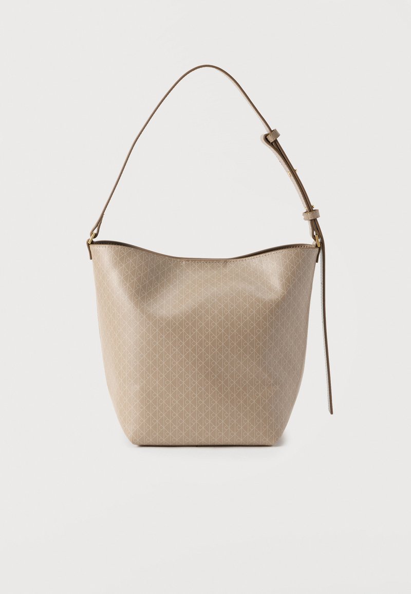 Τσάντα χειρός σε μπεζ με σχέδιο, με μαλακό, στρογγυλεμένο σχήμα, έναν ρυθμιζόμενο ιμάντα και χρυσούς μεταλλικούς εξαρτήματα. Η υφή είναι λεία και γυαλιστερή.