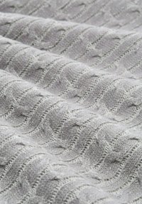 Tissu tricoté gris clair avec un motif de vagues en relief, présentant des fibres texturées et des mailles lisses et en jersey alternées.