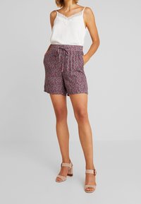 Camisole blanche avec bordure en dentelle associée à un short floral violet doté d'une taille élastique et de poches latérales. Sandales à talons hauts beiges.