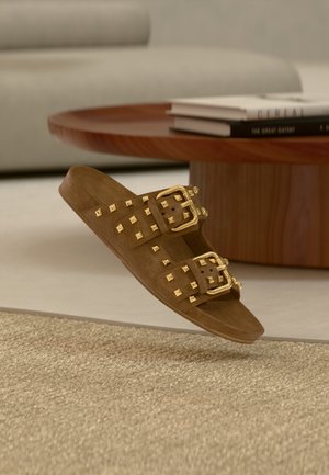 Sandale slide en daim marron avec doubles boucles dorées et clous carrés dorés, dotée d'un design à bout ouvert et d'une semelle plate.