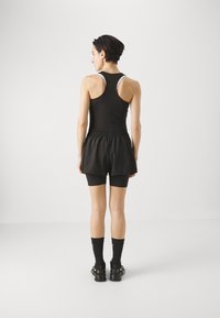 Ático deportivo negro con diseño de espalda nadadora, combinado con pantalones cortos atléticos negros. Material de neopreno con cinturilla elástica. Calcetines negros y sandalias.