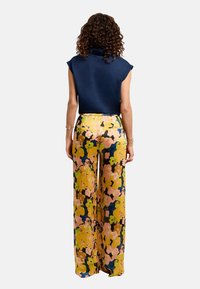 Top de manga corta color azul marino con cuello alto, combinado con pantalones de pierna ancha que presentan un colorido patrón floral en amarillo, rosa y azul.