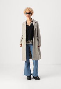 Cappotto grigio in lana con un design strutturato, abbinato a un top nero e una camicia con stampa leopardata, jeans blu a zampa d'elefante e scarpe nere chunky.