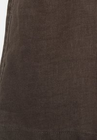 Közelkép sötétbarna, texturált anyagról, látható varrással a bal és alsó szél mentén.