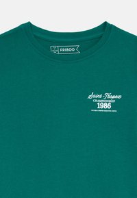 Žalias medvilninis marškinėliai su apvaliu iškirpimu. Savybė - balta užrašas "Saint-Tropez Championship 1986" ir sklandžią, minkštą tekstūrą.