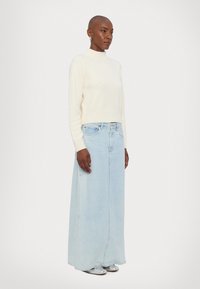 Krémový sveter s vysokým výstrihom, skombinovaný so svetlo modrou denimu maxi sukňou. Má uvoľnený strih a strieborné topánky. Minimalistický dizajn.
