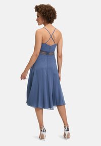 Une robe bleue avec un corsage ajusté, des détails en dentelle à la taille, et une jupe évasée qui tombe à mi-mollet. Elle présente des bretelles fines en croix et une texture lisse.