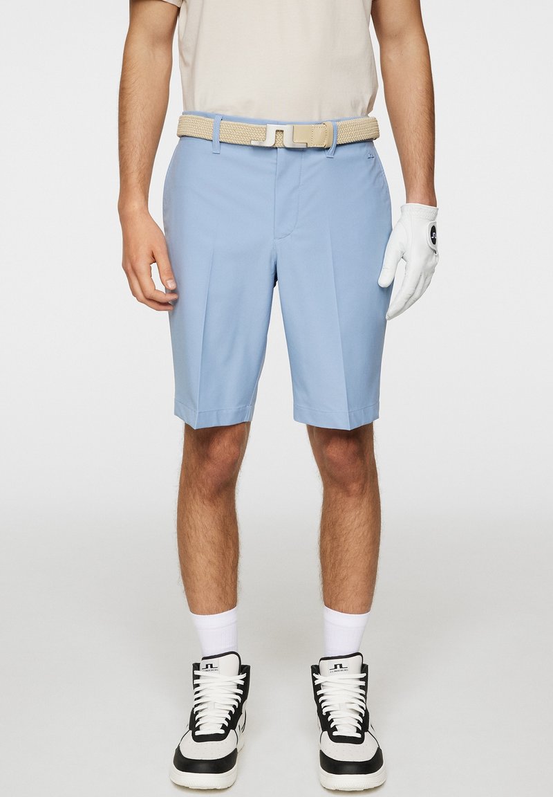 Ljusblå golfshorts i slätt tyg, med en skräddarsydd design och veck, tillsammans med ett beiget vävt bälte. Vita handskar och sneakers.