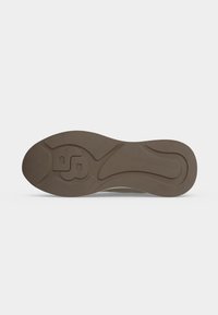 Semelle de chaussure en caoutchouc marron avec un motif texturé et un dessin en relief stylisé en forme de «B» près du talon, vue par en dessous.