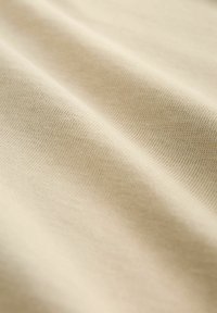 Tejido texturizado beige con un fino patrón de canalé, que muestra suaves pliegues y suavidad, enfatizando su ligereza y apariencia suave.